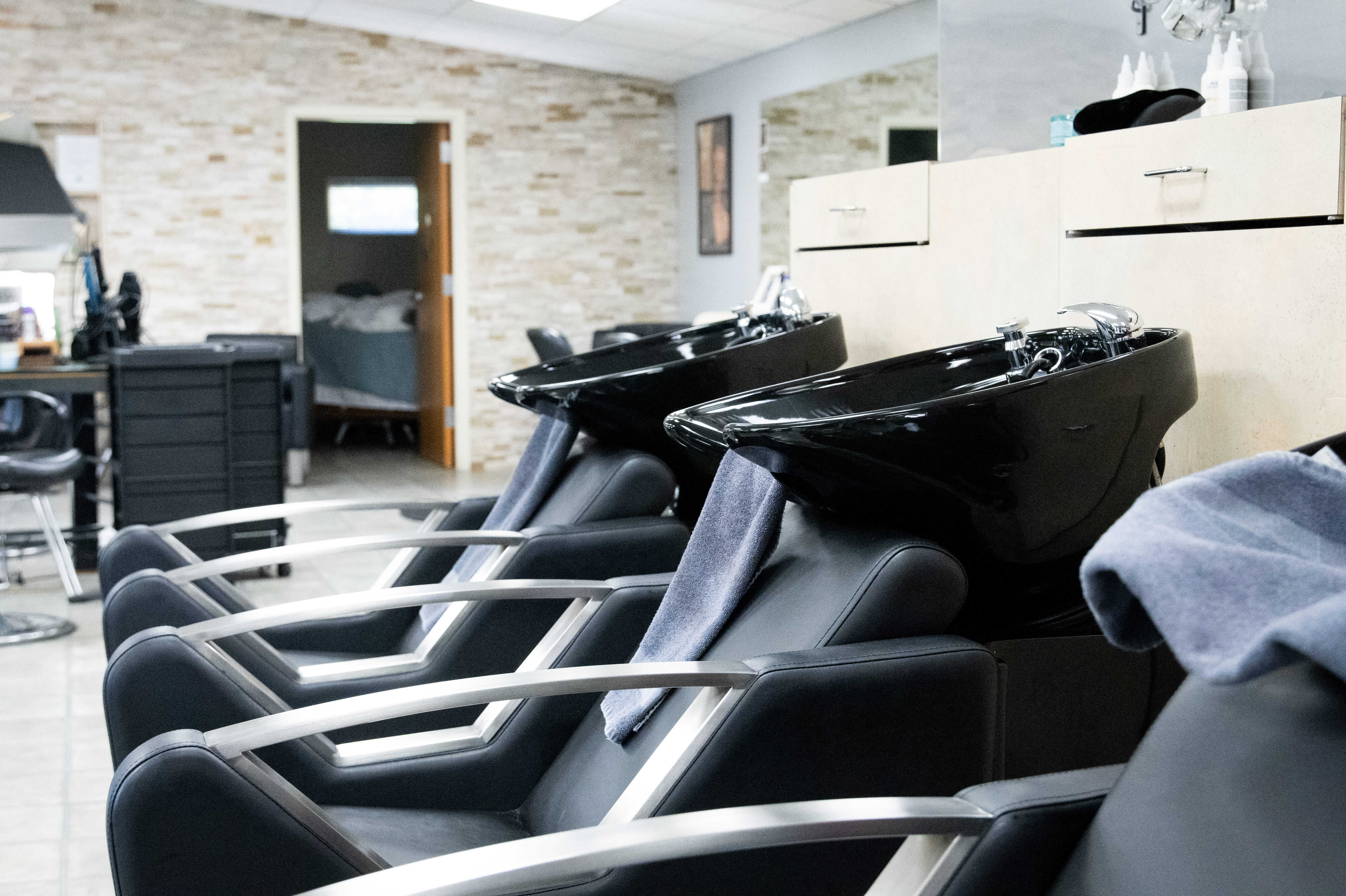 Three black salon shampoo chairs and sinks are lined up in a modern hair salon, with towels draped over the sinks—perfect for clients getting fresh hair color or extensions.